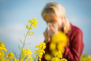 Woman blowing her nose in a field of flowers | Featured Image for the Is your Asthma Worse at Night? Night Time Asthma Relief Tips Blog by Wenatex.