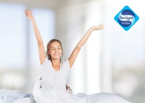 Woman sitting up in bed and stretching | Featured image for Sanitized® for a more hygienic and healthy sleep.