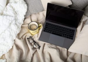 Laptop, glasses and tea on a bed | Featured image for The Importance of Your Sleep Environment blog from Wenatex.