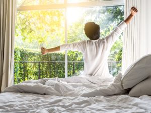 Man waking up in the bed and stretching | Featured image for How Does Lack of Sleep Affect Your Immune System?