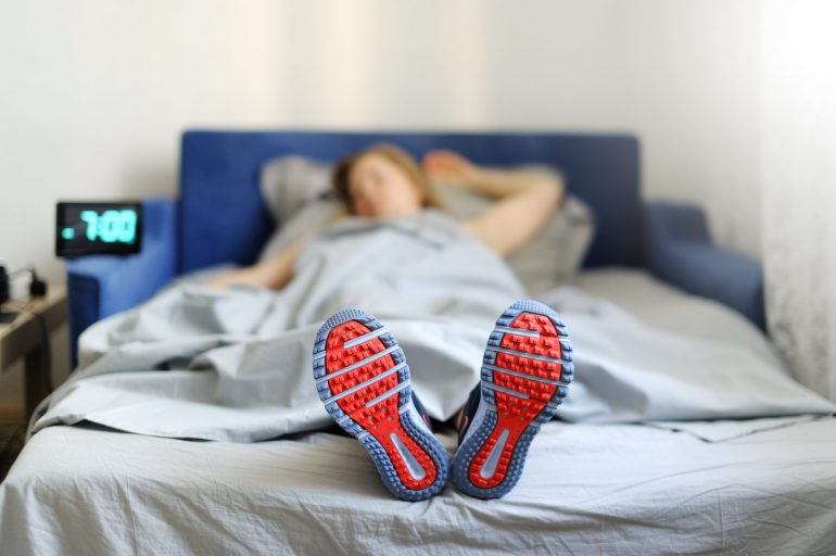 Photo of a woman lying in bed with her sneakers on | Featured image for Understanding the Relationship Between Sleep and Exercise blog from Wenatex.