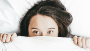 Woman covering face with a blanket while looking straight into the camera | Featured Image for Quality Sleep is Fundamental To Good Health But Is It A Good Investment? blog on Wenatex