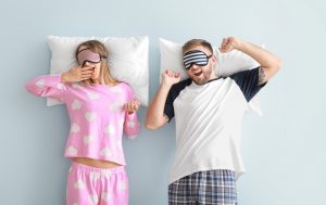 Two people yawning while resting on pillows | Featured image for How your sleep environment can affect sleep quality.