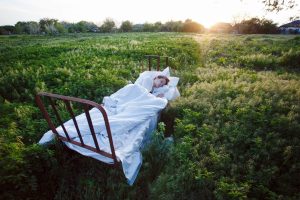 Woman sleeping on a bed in a field | Featured image for Wenatex’s Herbal Sleep Aids Blog.