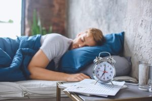 Man Sleeping in Bed with Alarm on the Bedside Table | Featured image for Wenatex’s Science of Sleep: Understanding Your Sleep Cycle Blog.