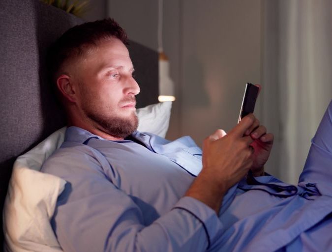 Person on phone in bed | Featured Image for the Light and Sleep Blog by Wenatex.