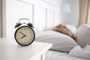 Woman sleeping in bed with an alarm clock sitting on a night stand - Featured image for the "What is the Circadian Rhythm and Why is it Important?" blog post.