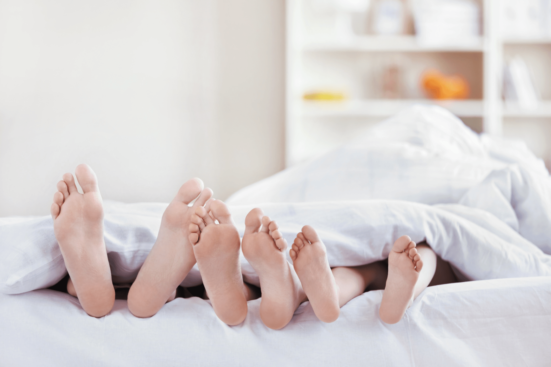 Three pairs of feet sticking out from under a doona - Featured image for the "How Much Sleep Do You Need" blog post.