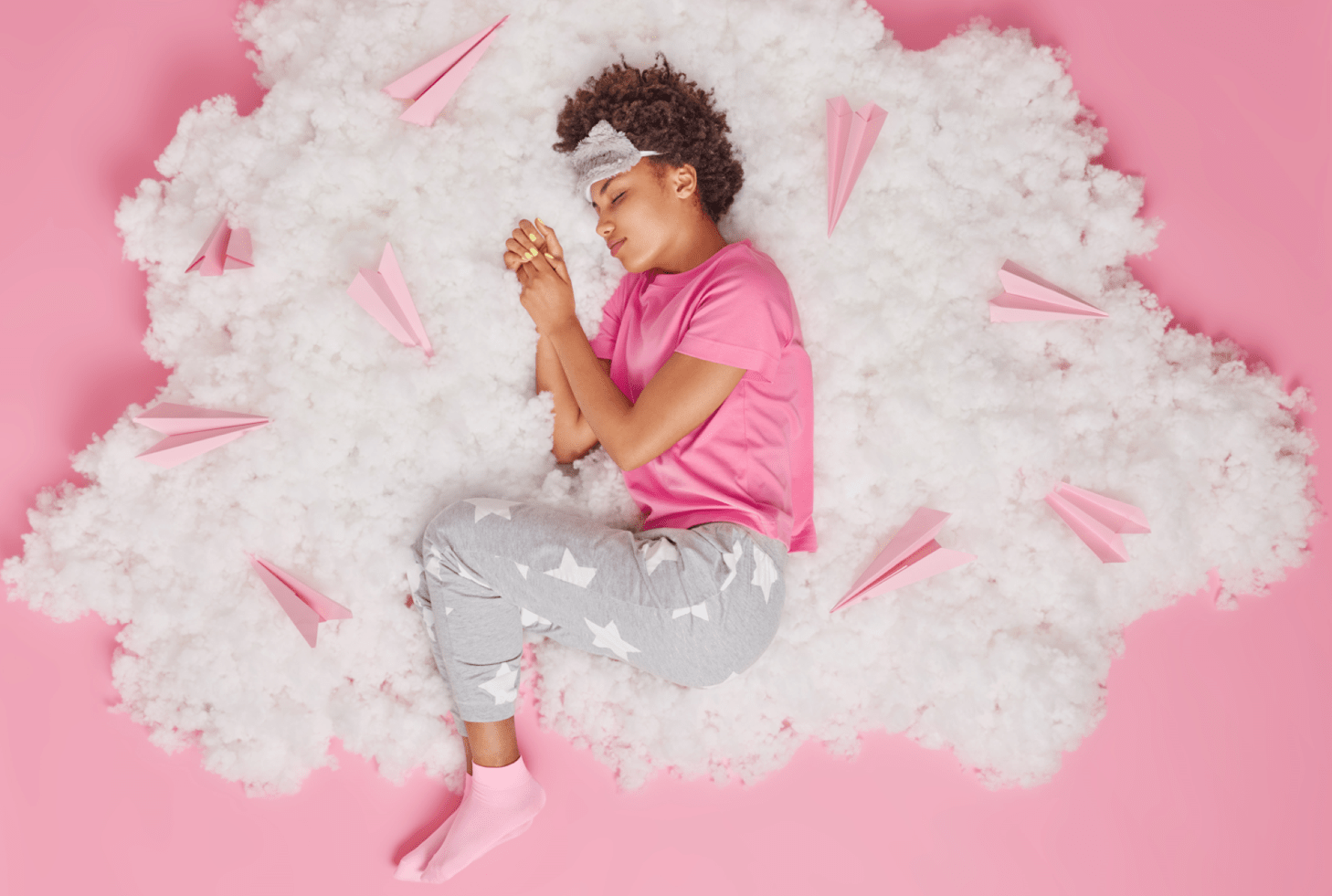 A woman sleeping on a cloud made of fluff, surrounded by pink paper airplanes - Featured image for the "How to Get More Deep Sleep" blog post.