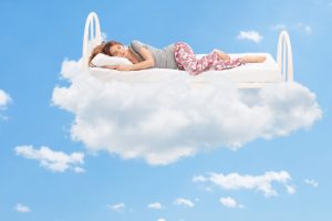 Woman sleeping on a comfortable bed in the clouds | Featured image for the Vivid Dreams – Exploring What They Are & Why They Happen blog from Wenatex.